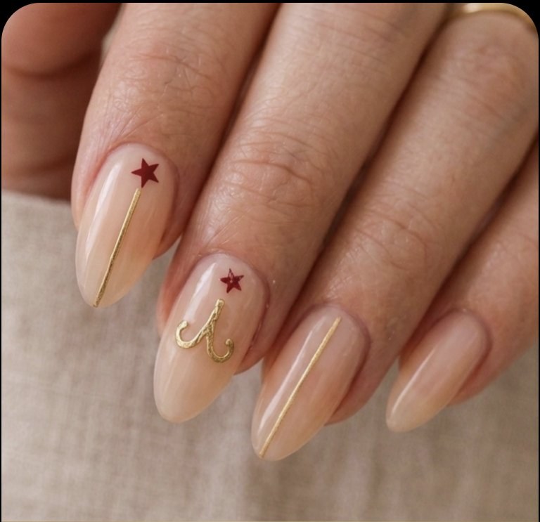 Minimal Aries manicure with sheer nude almond nails, fine gold lines, Aries glyph and crimson star details.