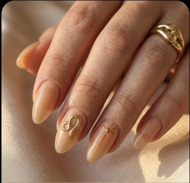 Minimal Leo manicure with honey-beige tapered almond nails, molten gold accents, Leo glyph and warm amber details.